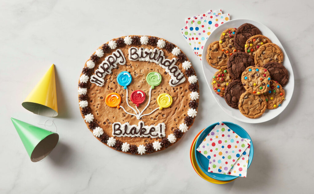 A flat lay comprising of party hats, Great American Cookie Cake with 
